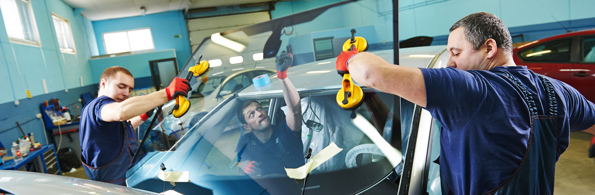 Two technicians installing a new windshield with suction handles
