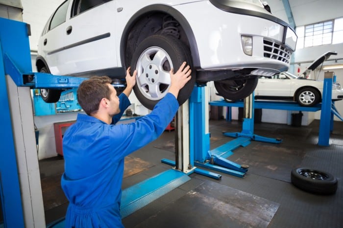 Mechanic fitting a tire onto a car raised on a shop lift