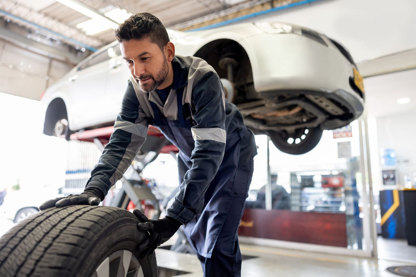 Mechanic changing a tire with a car on a lift behind him