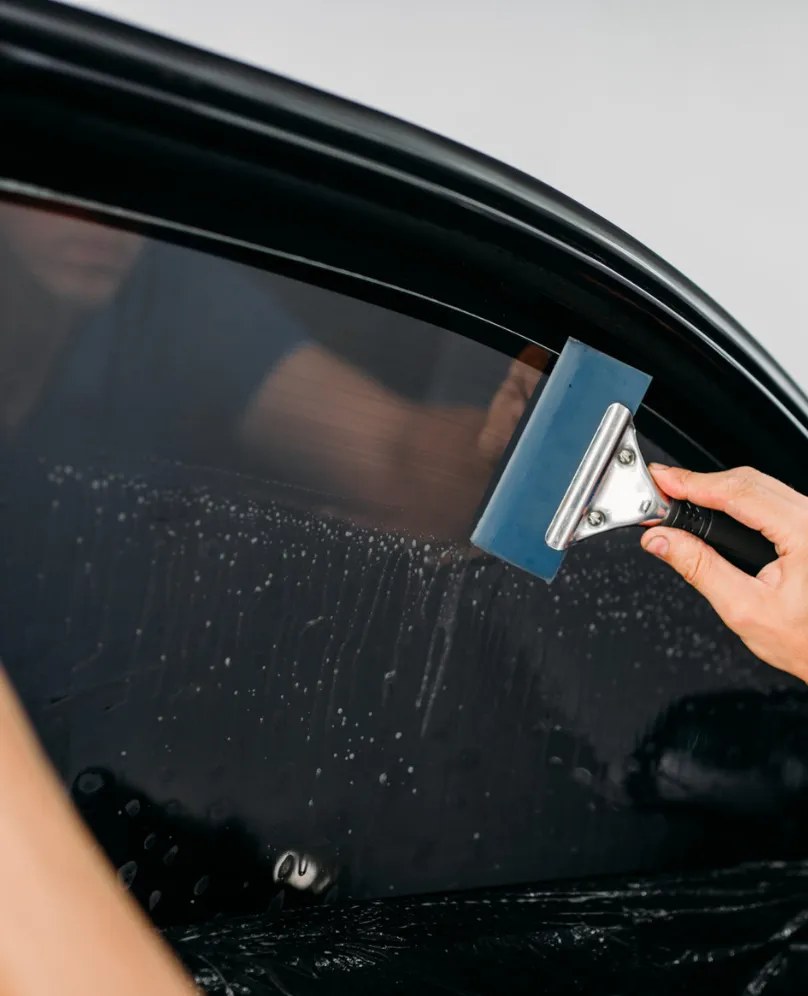 Close-up of tint film being finished on a car window with a blue squeegee
