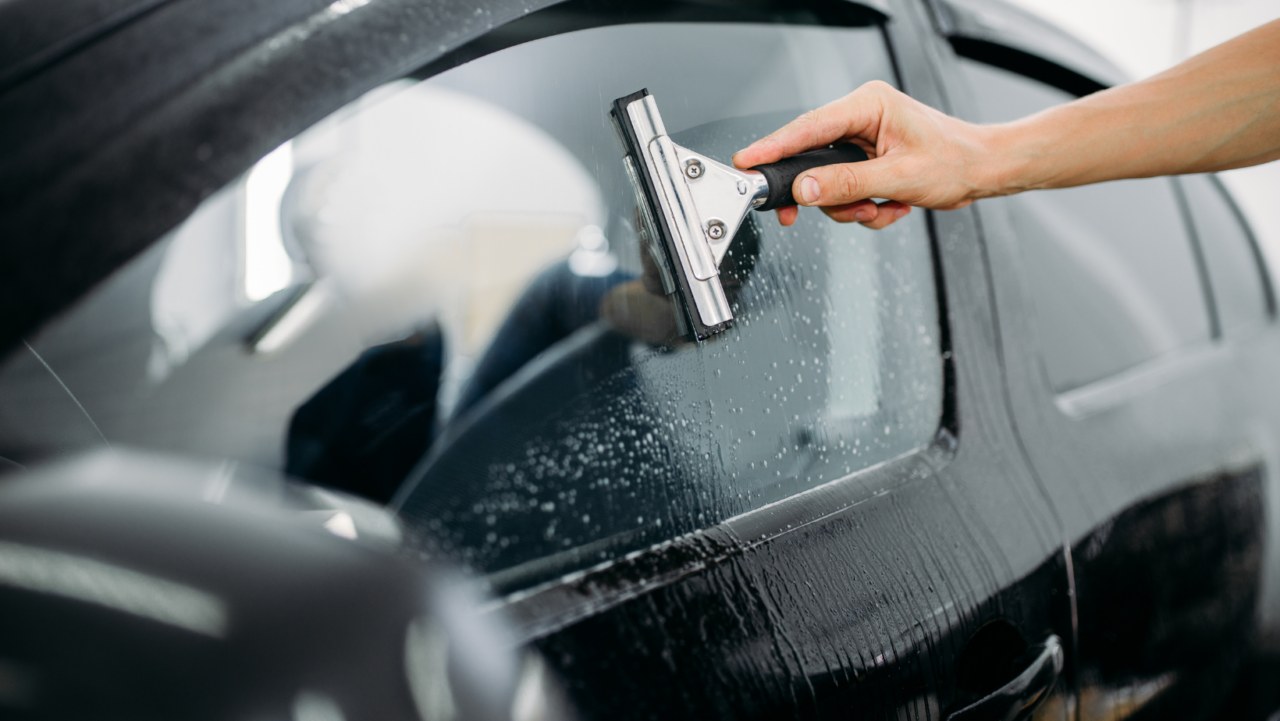 Hand using a squeegee to smooth tint film on a car window